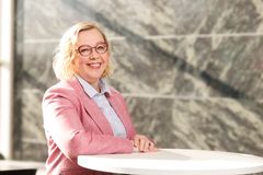 Jonna Järveläinen nojaa pöytään ja hymyilee arvokkaan näköisessä ympäristössä.